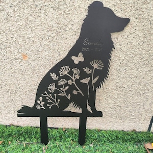 May include: Black metal silhouette of a dog, designed as a garden stake. The dog is decorated with floral and butterfly cutouts. The name "Sarah" and dates "2021-2022" are etched into the design. The stake is placed in green grass.