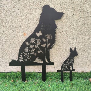 May include: Black metal garden stakes featuring a dog and a rabbit silhouette. The dog stake has the name "Sandy" and dates "2021-2023" etched into it. Both stakes are decorated with floral and butterfly cutouts.