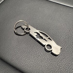 May include: A silver metal keychain shaped like a car. The keychain has a ring for attaching keys.