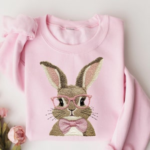 May include: Pink sweatshirt with a brown bunny wearing pink glasses and a bow tie embroidered on the front.