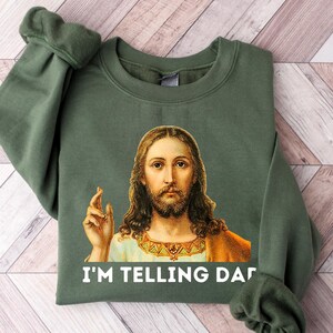 May include: A green sweatshirt with a picture of Jesus on it. The text "I'M TELLING DAD" is printed below the image.