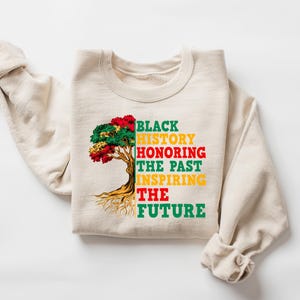 Pu&ograve; includere: Felpa color crema con la scritta "BLACK HISTORY HONORING THE PAST INSPIRING THE FUTURE" e una grafica ad albero rossa, verde e gialla. Le maniche sono drappeggiate di lato.