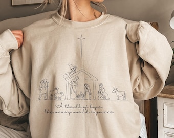 May include: A beige sweatshirt with a black line drawing of the nativity scene and the text "A thrill of hope, the weary world rejoices".