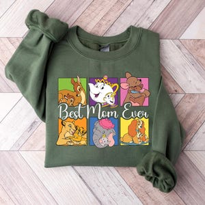 May include: Green sweatshirt with a colorful graphic featuring Disney characters and the text "Best Mom Ever." The graphic includes Bambi, Mrs. Potts, Roo, Simba, Dumbo, and Lady. The sweatshirt has long sleeves and a crew neck.