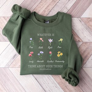 May include: An olive green sweatshirt with the text "WHATEVER IS" and "THINK ABOUT SUCH THINGS" with floral illustrations. The sweatshirt has a crew neck and long sleeves. The text "PHILIPPIANS 4:8" is also printed on the sweatshirt.