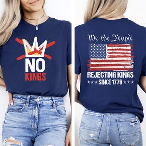 May include: Navy blue t-shirt with a graphic on the front that says "NO KINGS" with a crossed-out crown. The back of the shirt features an American flag design with the text "We the People REJECTING KINGS SINCE 1776."