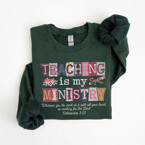 May include: A dark green sweatshirt with the words "TEACHING is my MINISTRY" in a colorful, patchwork design. The text "Whatever you do, work at it with all your heart, as working for the Lord Colossians 3:23" is printed below.