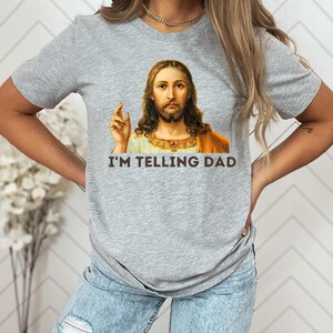 May include: A gray t-shirt with a picture of Jesus on it. The text "I'm telling Dad" is printed below the image.