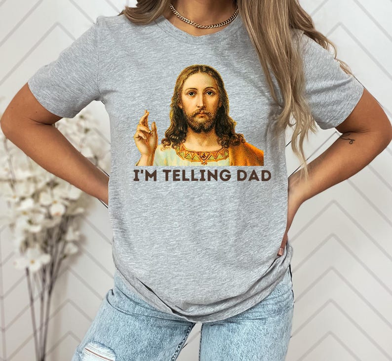 May include: A gray t-shirt with a picture of Jesus on it. The text "I'm telling Dad" is printed below the image.