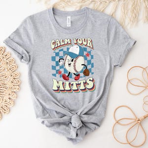 May include: Gray t-shirt with a retro baseball graphic and the text "Calm Your Mitts".