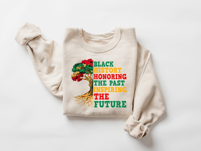 Pu&ograve; includere: Felpa color crema con la scritta "BLACK HISTORY HONORING THE PAST INSPIRING THE FUTURE" e una grafica ad albero rossa, verde e gialla. Le maniche sono drappeggiate di lato.