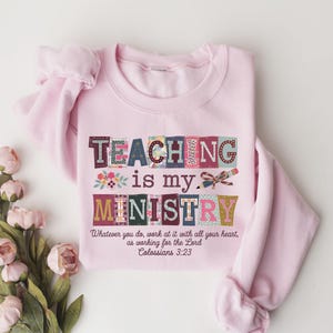 May include: A light pink sweatshirt with the words "TEACHING is my MINISTRY" in colorful block letters. The text "Whatever you do, work at it with all your heart, as working for the Lord Colossians 3:23" is printed below.