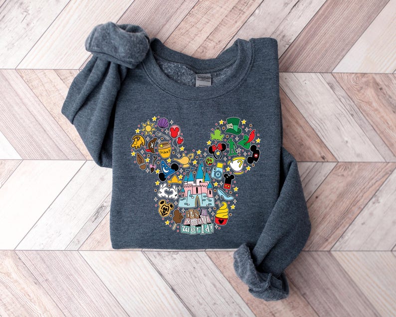 Puede incluir: Sudadera gris oscuro con un dise&ntilde;o colorido de la cabeza de Mickey Mouse. El dise&ntilde;o est&aacute; lleno de varios iconos tem&aacute;ticos de Disney, incluyendo un castillo, tazas de t&eacute; y la frase "it's a small world". La sudadera es de material suave.
