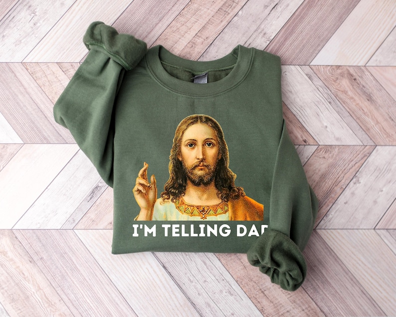 May include: A green sweatshirt with a picture of Jesus on it. The text "I'M TELLING DAD" is printed below the image.