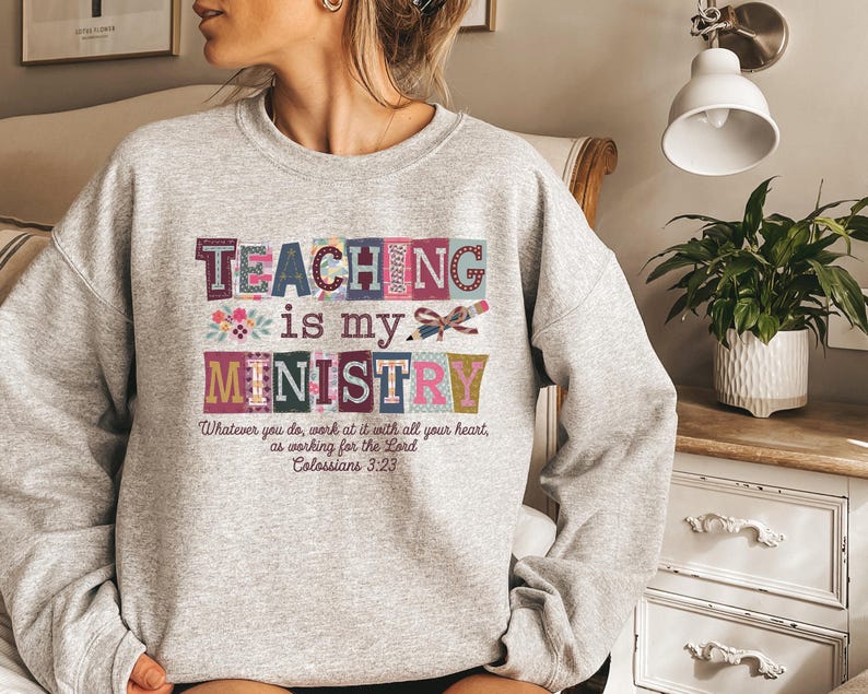 May include: A light gray sweatshirt with the words "TEACHING is my MINISTRY" in colorful block letters. Below the text is the Bible verse Colossians 3:23. The sweatshirt is a comfortable, casual style.