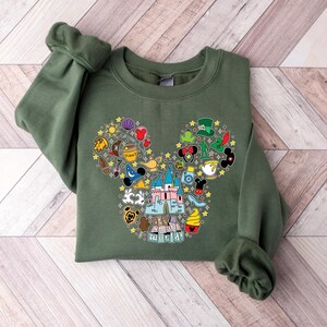 Puede incluir: Una sudadera verde oliva con un dise&ntilde;o de cabeza de Mickey Mouse lleno de coloridos iconos tem&aacute;ticos de Disney. El dise&ntilde;o incluye un castillo, sombreros y varias im&aacute;genes relacionadas con los personajes. La sudadera tiene mangas largas y cuello redondo.