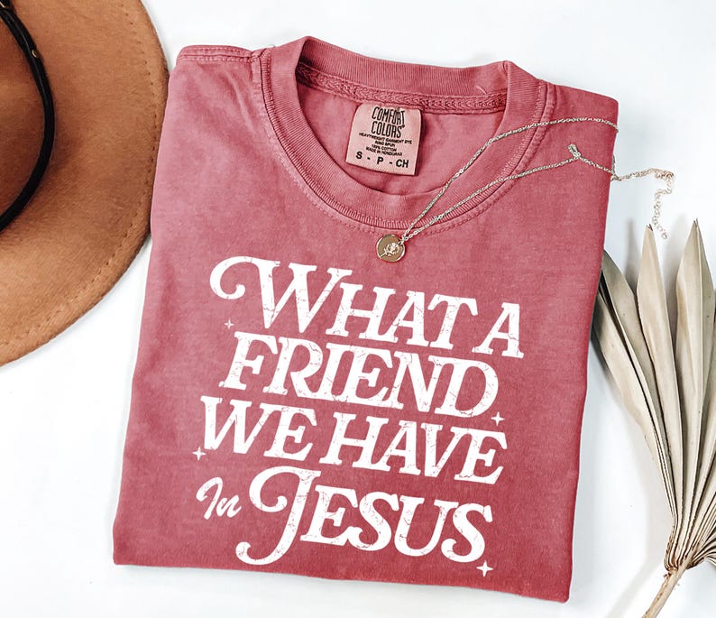 K&ouml;nnte beinhalten: Ein rotes T-Shirt mit einer wei&szlig;en Grafik im Vintage-Stil, auf dem "What a Friend We Have in Jesus" steht.
