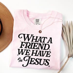 K&ouml;nnte beinhalten: Rosa T-Shirt mit schwarzem Text, der "What a Friend We Have in Jesus" lautet.