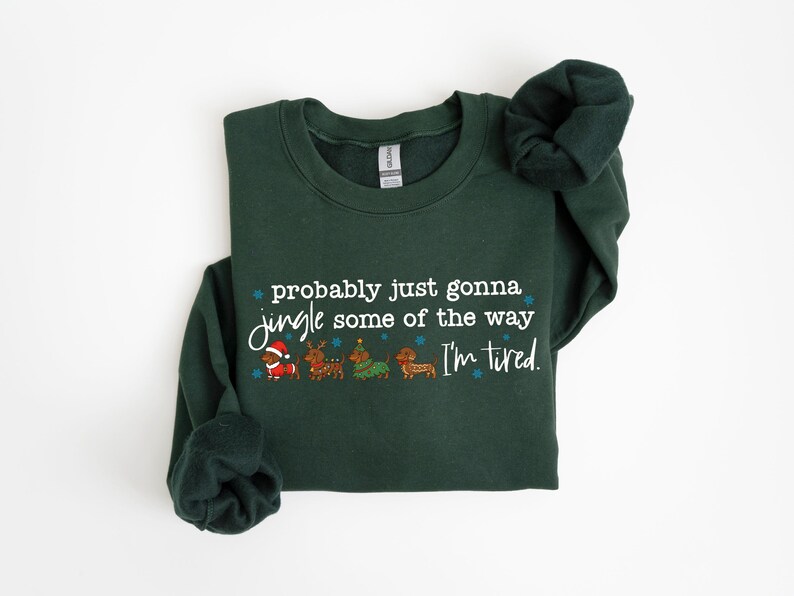 May include: A dark green sweatshirt with the text "probably just gonna jingle some of the way I'm tired." The graphic includes Santa, reindeer, a Christmas tree, and a dachshund. The sweatshirt has long sleeves.