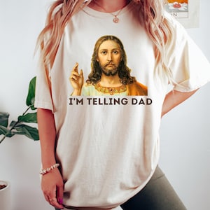 May include: A white t-shirt with a picture of Jesus on it. The text "I'M TELLING DAD" is printed below the image.
