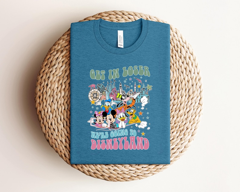 May include: A teal blue t-shirt with a graphic featuring Disney characters and the text "GET IN LOSER WE'RE GOING TO DISNEYLAND" in retro font. The design includes Mickey and Minnie Mouse, Donald Duck, and Goofy.