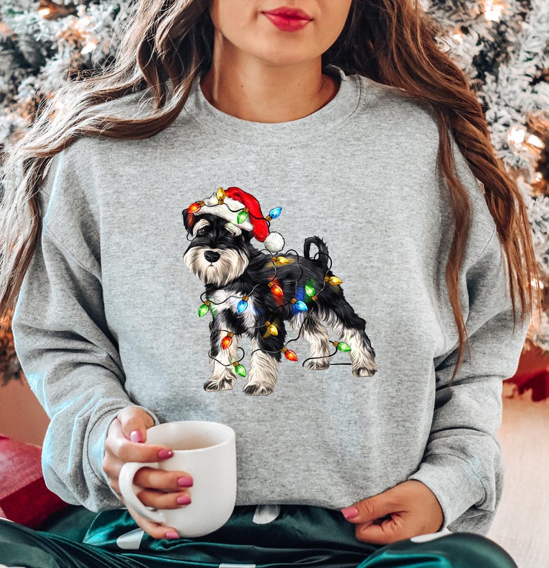 May include: A grey sweatshirt featuring a black and white miniature schnauzer wearing a Santa hat and tangled in Christmas lights.