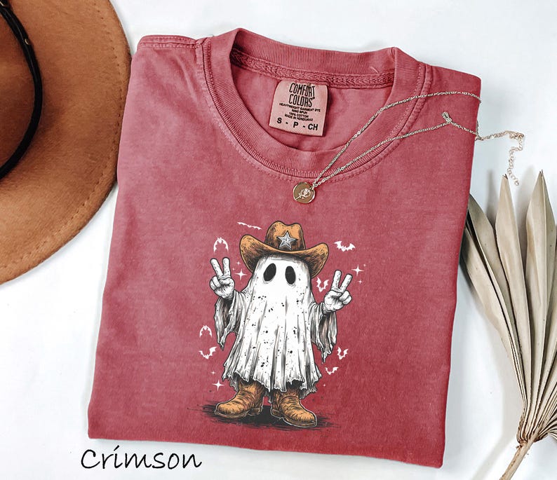 Pu&ograve; includere: T-shirt color cremisi con un fantasma dei cartoni animati che indossa un cappello e stivali da cowboy, che fa il segno della pace. La grafica &egrave; al centro della maglietta. Una collana d'oro &egrave; drappeggiata sulla maglietta. La maglietta &egrave; realizzata in materiale morbido.