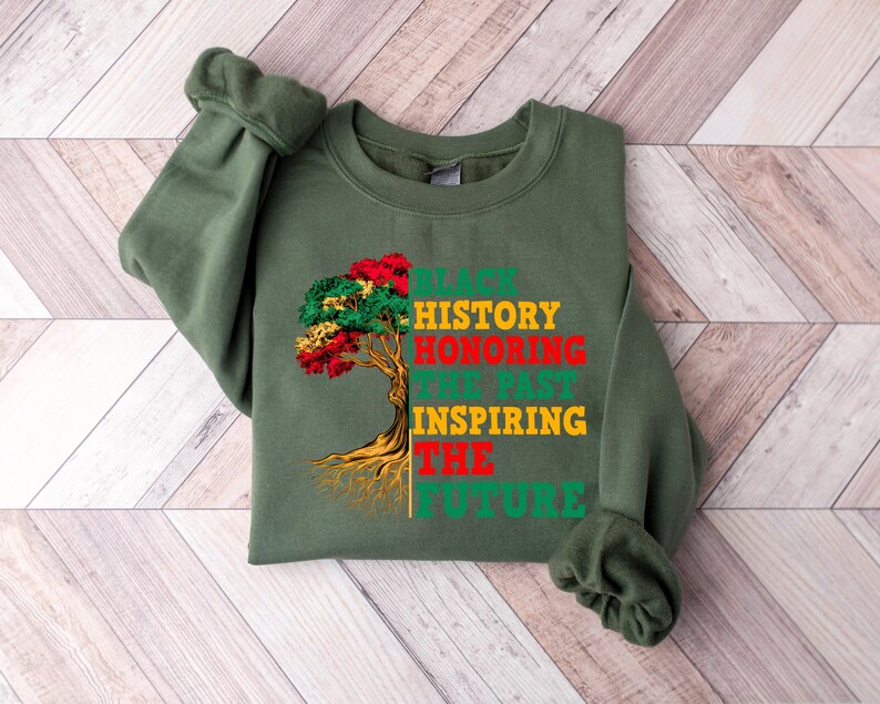 Pu&ograve; includere: Una felpa verde oliva con la scritta "BLACK HISTORY HONORING THE PAST INSPIRING THE FUTURE" in verde, rosso, giallo e verde. Una grafica ad albero con foglie rosse, gialle e verdi &egrave; a sinistra.