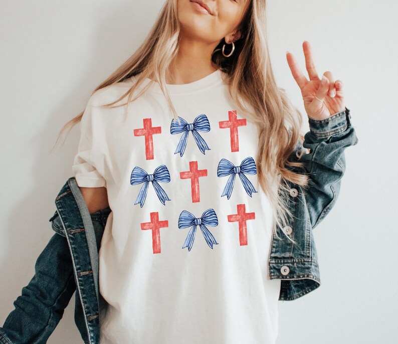 May include: White t-shirt featuring a repeated design of red crosses and blue bows.