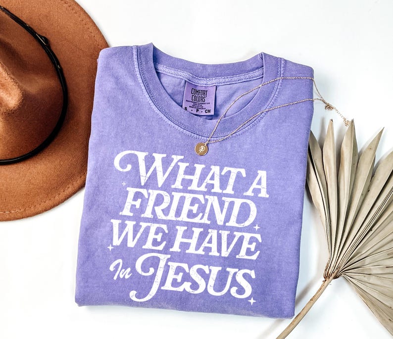 K&ouml;nnte beinhalten: Ein lavendelfarbenes T-Shirt mit dem Aufdruck "What a Friend We Have in Jesus" in Wei&szlig;. Das Shirt hat einen Used-Look und ist aus weichem, bequemem Stoff.