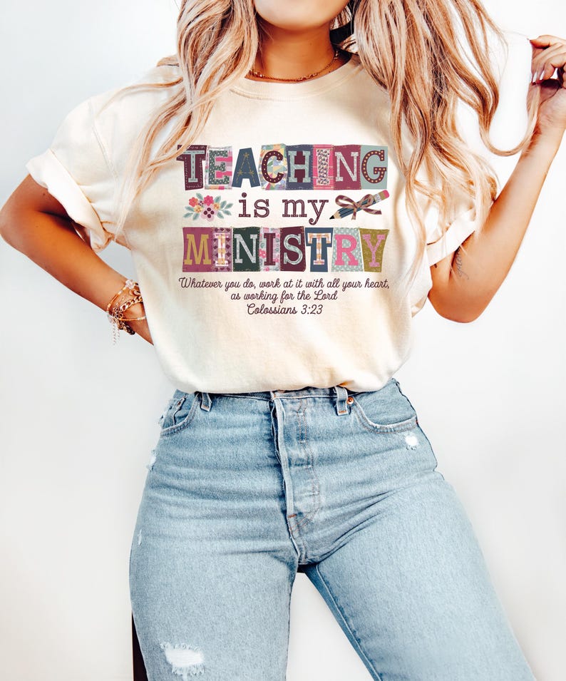 May include: Cream-colored t-shirt with the text "TEACHING is my MINISTRY" in a colorful, block-letter design. The shirt also features the Bible verse Colossians 3:23. The shirt is paired with light blue jeans.
