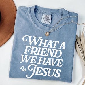 K&ouml;nnte beinhalten: Ein hellblaues T-Shirt mit einem wei&szlig;en, abgenutzten Aufdruck, der "What a Friend We Have in Jesus" lautet.