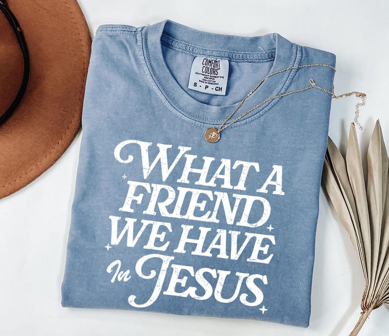 K&ouml;nnte beinhalten: Ein hellblaues T-Shirt mit einem wei&szlig;en, abgenutzten Aufdruck, der "What a Friend We Have in Jesus" lautet.