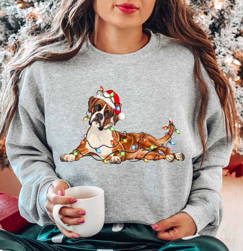 May include: A gray sweatshirt with a brown and white boxer dog wearing a Santa hat and surrounded by colorful Christmas lights.