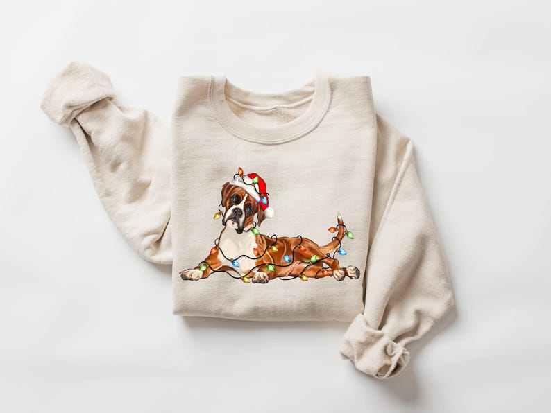 May include: A beige sweatshirt with a brown and white boxer dog wearing a red Santa hat and tangled in Christmas lights.