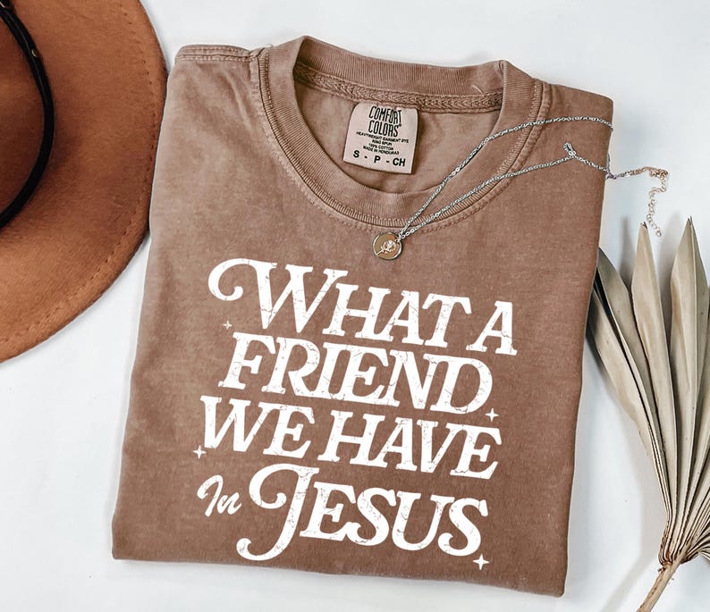 K&ouml;nnte beinhalten: Ein braunes T-Shirt mit einem wei&szlig;en, abgenutzten Aufdruck, der "What a Friend We Have in Jesus" lautet.