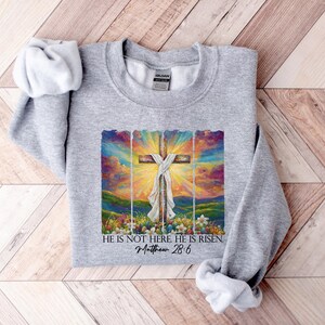 May include: Grey sweatshirt featuring a colourful painting of a cross with the text "He is not here He is risen. Matthew 28:6"