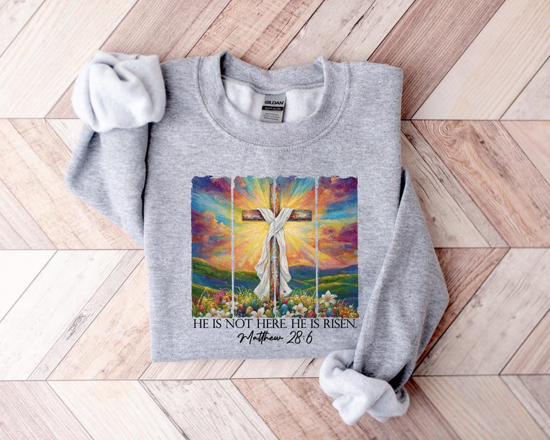 May include: Grey sweatshirt featuring a colourful painting of a cross with the text "He is not here He is risen. Matthew 28:6"