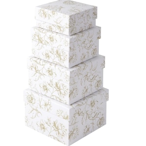 May include: A stack of five white gift boxes with lids. Each box is adorned with a gold floral pattern. The boxes are rectangular and vary in size, creating a tiered effect. The floral design adds a touch of elegance.