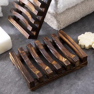 May include: Wooden soap dish with a dark brown finish. The dish has a slatted design with curved supports, allowing for drainage. The soap dish is designed to hold a bar of soap and is made of natural wood.
