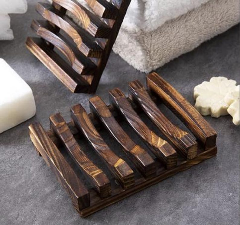 May include: Wooden soap dish with a dark brown finish. The dish has a slatted design with curved supports, allowing for drainage. The soap dish is designed to hold a bar of soap and is made of natural wood.