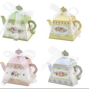 May include: Four decorative teapot-shaped boxes in pastel colors: green, yellow, pink, and blue. Each box features floral designs, gold accents, and a white ribbon bow. The boxes are ideal for small gifts or party favors.