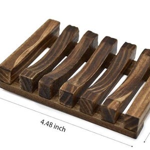 May include: A dark brown wooden soap dish with a slatted design. The dish measures 4.48 inches long, 3.15 inches wide, and 0.82 inches high. The soap dish is made of wood and has a natural finish.