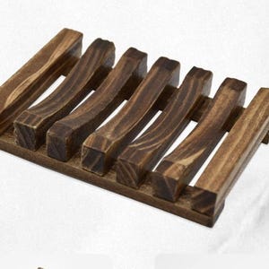 May include: A dark brown wooden soap dish with a rectangular base and seven curved, parallel slats. The wood grain is visible, and the dish is designed to allow water to drain, extending the life of the soap.