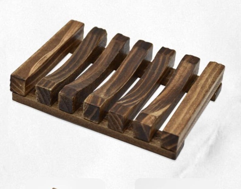 May include: A dark brown wooden soap dish with a rectangular base and seven curved, parallel slats. The wood grain is visible, and the dish is designed to allow water to drain, extending the life of the soap.