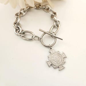 May include: A silver chain bracelet with a toggle clasp and a silver Saint Christopher medal charm.