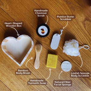 Puede incluir: Un conjunto de productos para el baño y el cuerpo, que incluye una caja de madera en forma de corazón, un cepillo corporal de bambú, un exfoliante de castañas, una piedra pómez, una esponja vegetal, jabón de cúrcuma y una esponja facial de fibra natural.
