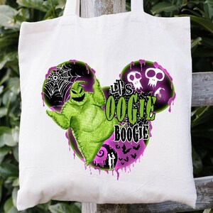 May include: A white tote bag with a green and black Oogie Boogie design and the text "Let's Oogie Boogie". The design includes a spiderweb, skulls, and a purple dripping effect. The bag is hanging on a wooden fence.