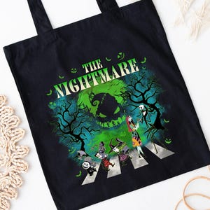 Pode incluir: Sacola preta com um gr&aacute;fico de "O Estranho Mundo de Jack". O design mostra personagens atravessando uma faixa de pedestres com um fundo verde e azul assustador. As palavras "THE NIGHTMARE" s&atilde;o impressas acima da imagem.