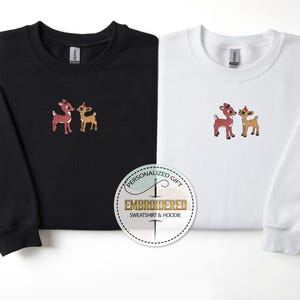Peut inclure: Deux sweat-shirts noirs et blancs avec des images brod&eacute;es d'un couple de rennes rouge et brun. Le texte "Cadeau personnalis&eacute;" et "Sweat-shirt et sweat &agrave; capuche brod&eacute;" est sur un autocollant rond blanc.